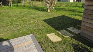 A grassy backyard with a wooden deck, a fenced area, and a house in the background. - Villa Martic in Biscarrosse (Biscarrosse)
