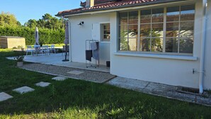A white house with a tiled roof, a large window, and a small patio area with outdoor furniture. - Villa Martic in Biscarrosse (Biscarrosse)