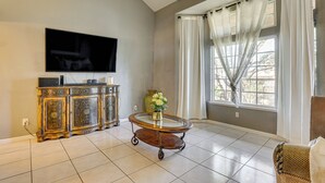 A living room with a flat-screen TV, a wooden cabinet, a glass coffee table, and a window with curtains. - Private Pool, Grill & Fenced Yard: Las Vegas Home (Las Vegas)