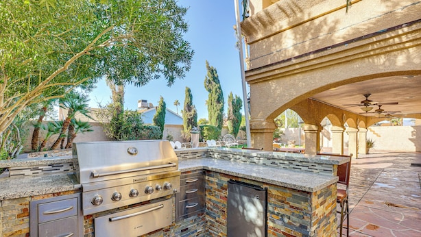An outdoor kitchen with a built-in grill, oven, and refrigerator, surrounded by a stone wall and greenery. - Private Pool, Grill & Fenced Yard: Las Vegas Home (Las Vegas)