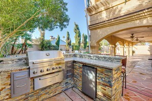 An outdoor kitchen with a built-in grill, oven, and refrigerator, surrounded by a stone wall and greenery. - Private Pool, Grill & Fenced Yard: Las Vegas Home (Las Vegas)