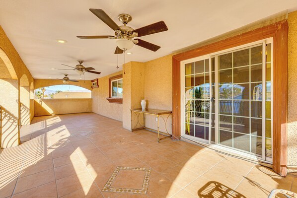A covered patio area with ceiling fans, a table, and a sliding glass door leading to an outdoor space. - Private Pool, Grill & Fenced Yard: Las Vegas Home (Las Vegas)