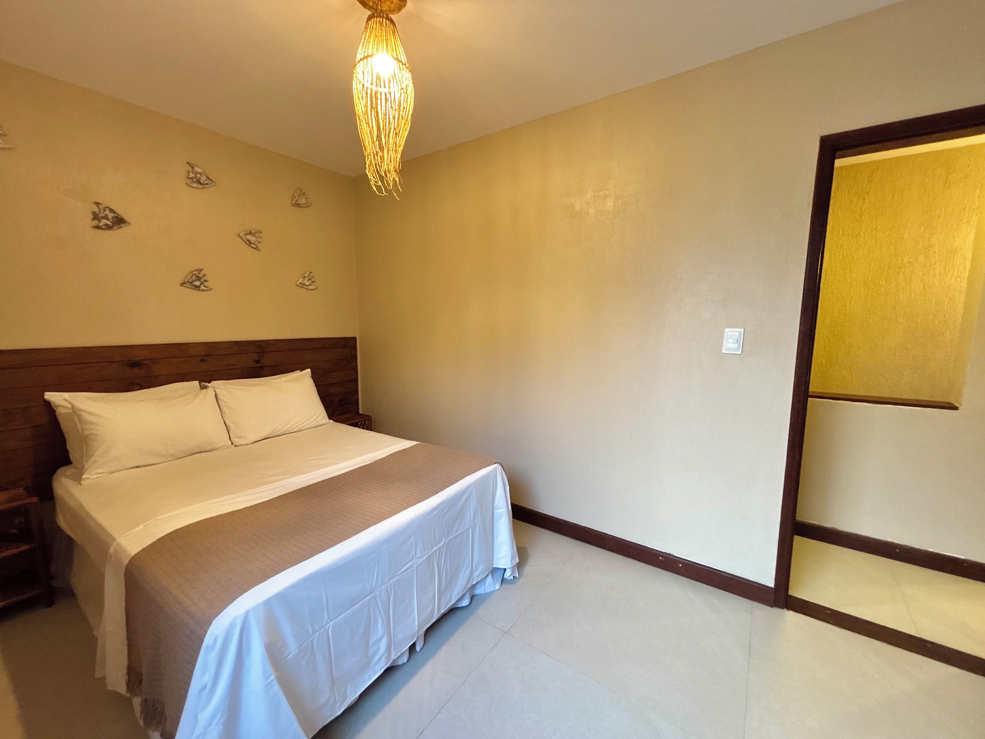 A bedroom with a wooden headboard, a bed with white bedding, a hanging light fixture, and a wall with decorative fish motifs.