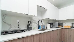 Una cocina moderna con armarios blancos, un protector contra salpicaduras de mármol y un microondas empotrado.