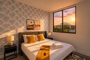 A hotel room with a large bed, two bedside lamps, a window with a sunset view, and patterned wallpaper. - King Bed 2B/2Ba Oasis minutes to Brickell 6 guests (Miami)