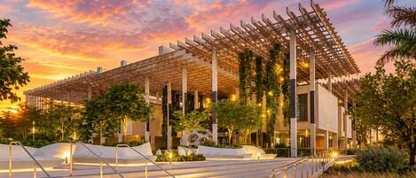 A modern building with a wooden pergola, outdoor stairs, and greenery.