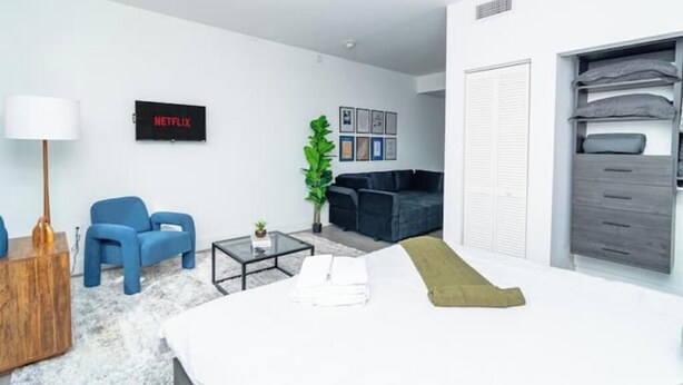 Una sala de estar moderna con un sofá, sillas, una mesa de centro y un televisor que muestra 'NETFLIX'.