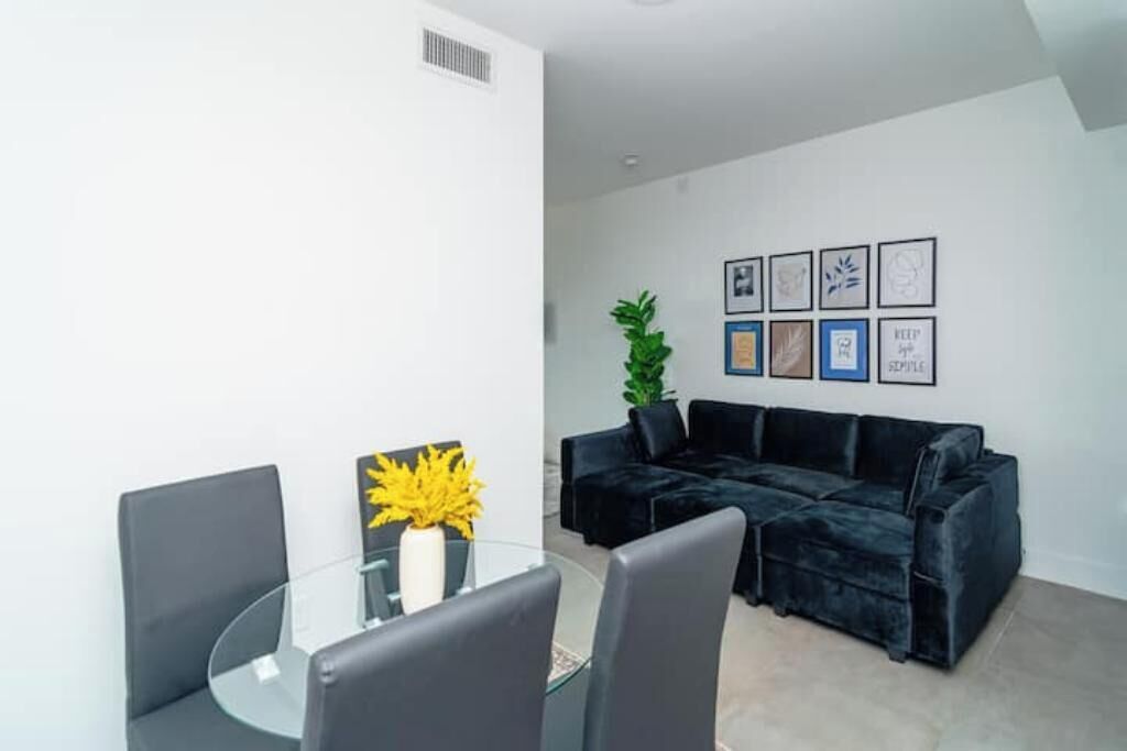 Un salon moderne avec une table en verre, des fauteuils gris, un canapé noir et des œuvres d’art encadrées accrochées au mur.
