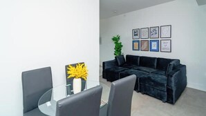 Una sala moderna con una mesa de vidrio, sillas grises, un sofá negro y obras de arte enmarcadas en la pared.