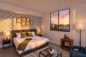A hotel room with a bed, bedside lamps, a view of a sunset, and a framed picture on the wall. - King Bed brand new safe Oasis minutes to Brickell (Miami)