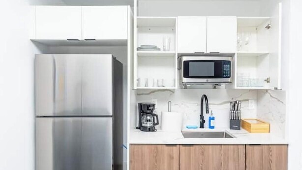 Una cocina moderna con un refrigerador de acero inoxidable, un microondas y una cafetera sobre la encimera.