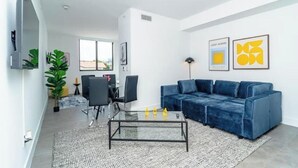 A modern living room with a blue sofa, a glass coffee table, and artwork on the walls.