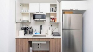 Una cocina moderna con armarios blancos, microondas, pileta y refrigerador de acero inoxidable.