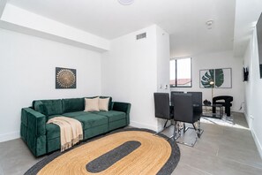 A modern living room with a green sofa, a coffee table, and a dining area with chairs. - King Bed brand new safe Oasis minutes to Brickell (Miami)