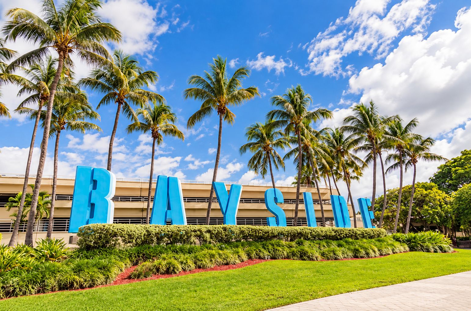 A hotel sign with the name 'BAYSIS' in large blue letters, surrounded by palm trees and a clear sky.