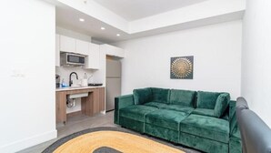 A compact living space with a green sofa, a kitchen area, and a decorative wall piece.