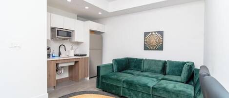 Un espacio habitable compacto con un sofá verde, una zona de cocina y un adorno de pared.