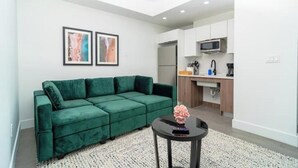 A modern living room with a green sofa, a small round table with a vase, and a kitchen area with white cabinets and appliances. - King Bed brand new safe Oasis minutes to Brickell (Miami)