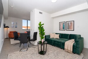 A modern living room with a green sofa, a dining area with a table and chairs, and a large window providing a view. - King Bed brand new safe Oasis minutes to Brickell (Miami)