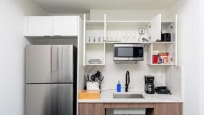Une cuisine compacte équipée d’un réfrigérateur en acier inoxydable, d’un four à micro-ondes et d’une machine à café.