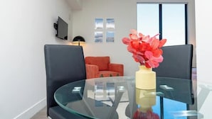 Un salon moderne avec une table en verre, des chaises noires et orange, un vase rempli de fleurs rouges et un téléviseur fixé au mur.