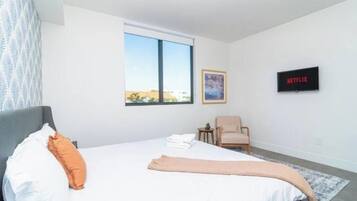 Une chambre à coucher avec un lit, une chaise, une petite table, une fenêtre et un téléviseur fixé au mur.