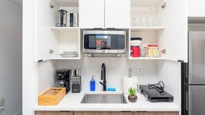 Cocina compacta equipada con microondas, lavamanos y utensilios de cocina.