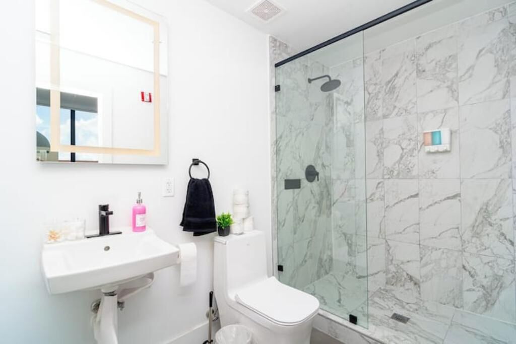 Un baño con lavamanos blanco, inodoro y cabina de ducha de vidrio con paredes de mármol.