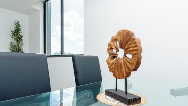 Una habitación moderna con una mesa de vidrio, una escultura de madera decorativa y vistas de la ciudad a través de amplias ventanas.
