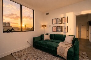A green sofa with a throw blanket, a patterned rug, and framed artwork on the wall.