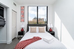 A hotel room with a bed, two bedside tables, a window with a view of buildings, and a door with a closet.