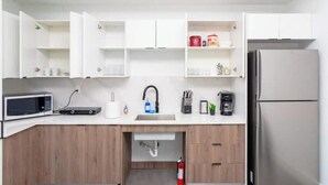 Una cocina moderna con armarios blancos, un refrigerador de acero inoxidable, un microondas y una cafetera.