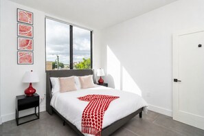 A modern bedroom with a bed, bedside tables, and a view of the outdoors.
