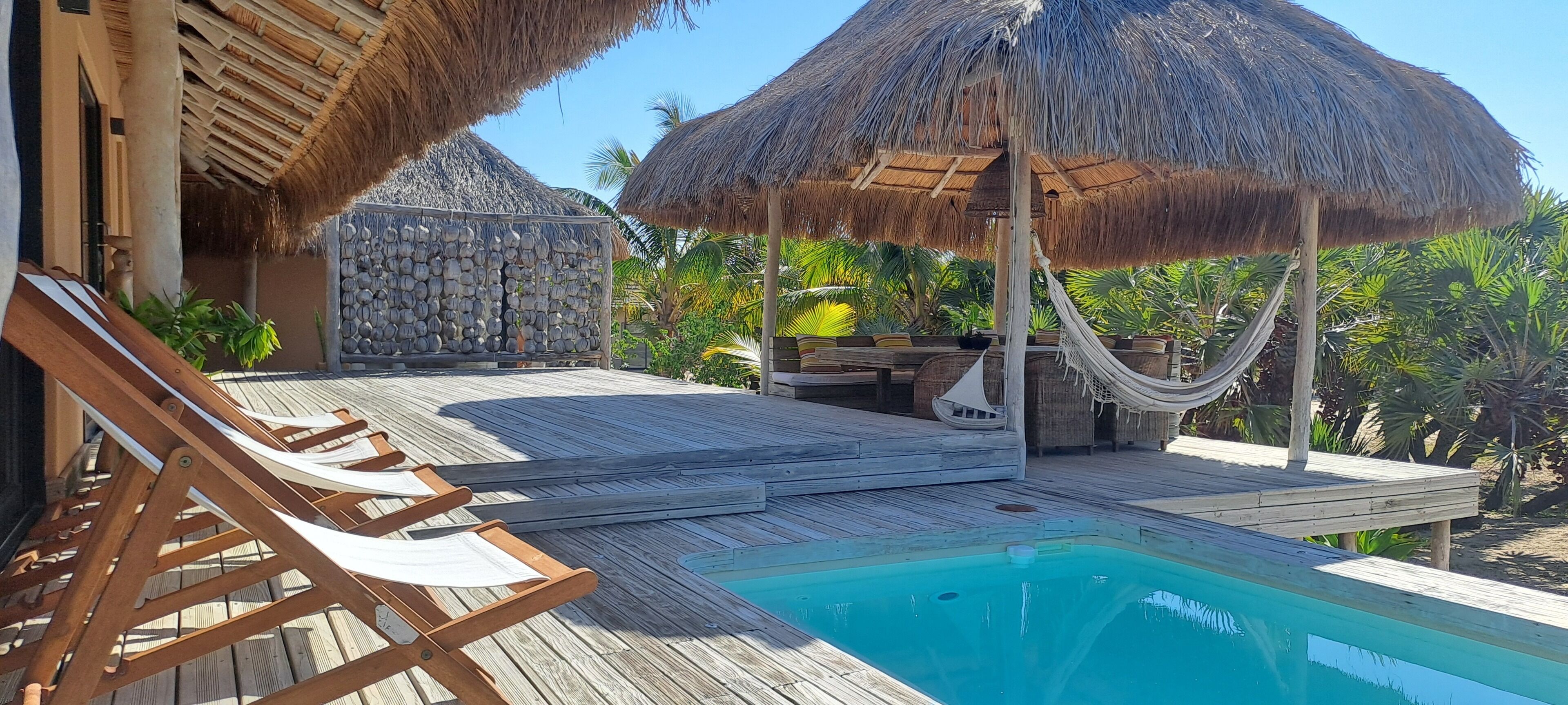 En træterrasse med pool, liggestole og stråtækte parasoller.