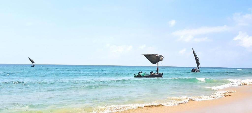 A beach with calm waters, a sandy shore, and three boats with sails.