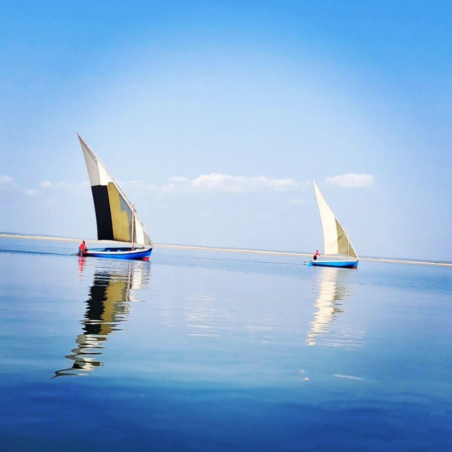 Two sailboats on calm water with a clear sky.