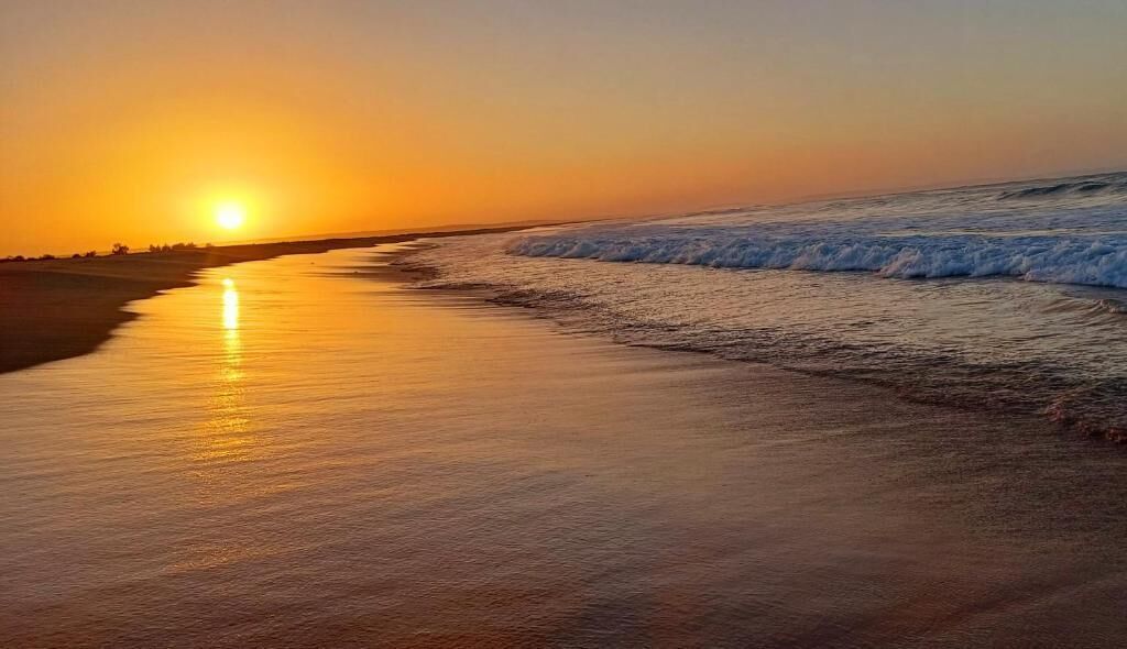 Una playa al atardecer con olas mansas lamiendo la orilla.