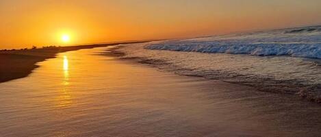 Una playa al atardecer con olas mansas lamiendo la orilla.