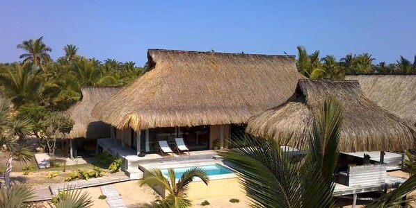 A resort with thatched-roof structures, a pool, and lounge chairs. - Sunset Villa - Luxury Beachfront Villa with Private Pool by Karula Sand Villas (Inhambane)
