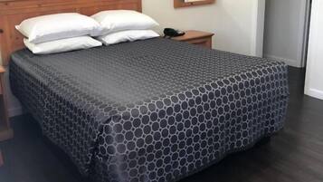 Una cama bien hecha con una colcha estampada, un cabecero de madera, una mesita de noche con un teléfono y un cuadro de flores enmarcado en la pared.