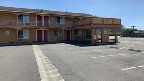 Un motel doté d’une entrée principale, de plusieurs chambres et d’un espace couvert agrémenté d’une rambarde.