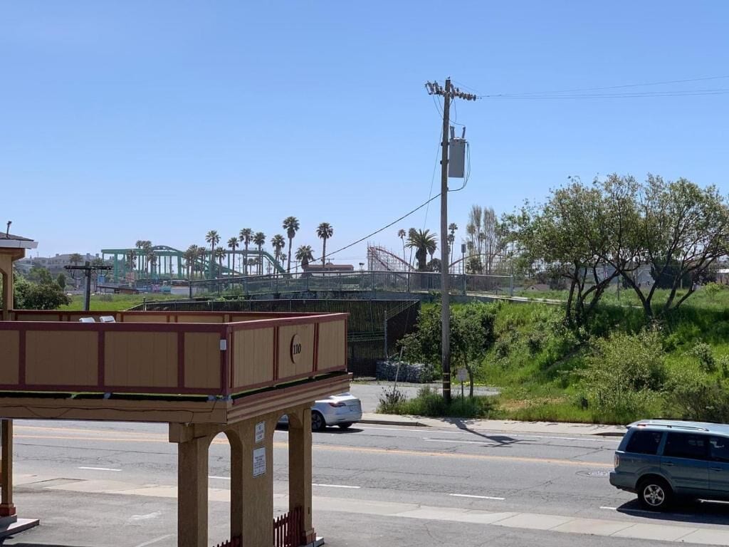 Vista de una calle con un edificio que presenta una gran estructura de madera, posiblemente un quiosco o puesto, y una clara vista de un puente y palmeras al fondo.
