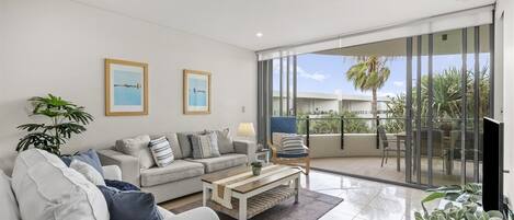 Una sala moderna con sofá, una mesa de centro y vistas a un balcón con mobiliario exterior.