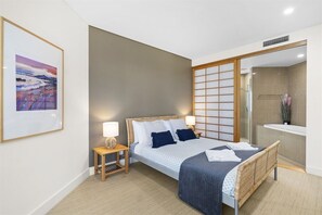 A modern hotel room with a bed, bedside tables, a large mirror, and a bathroom with a shower and sink.