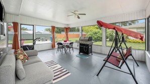 Une terrasse couverte avec un canapé, un barbecue, une balançoire et une table avec des chaises.