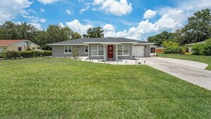 Une maison de plain-pied avec une porte d’entrée rouge, un garage et une pelouse bien entretenue.