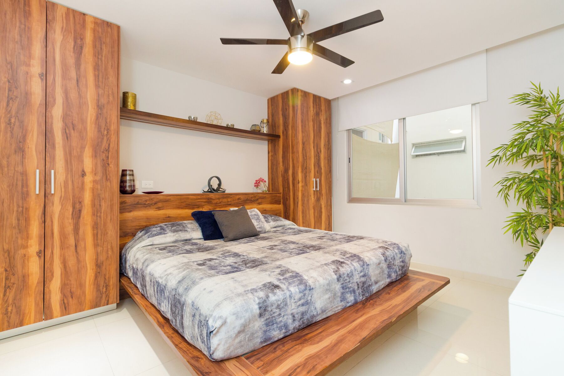 A bedroom with a bed, wooden wardrobe, ceiling fan, and a window.