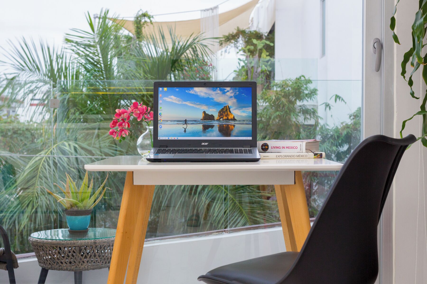 A laptop on a small table with a view of a beach and palm trees.