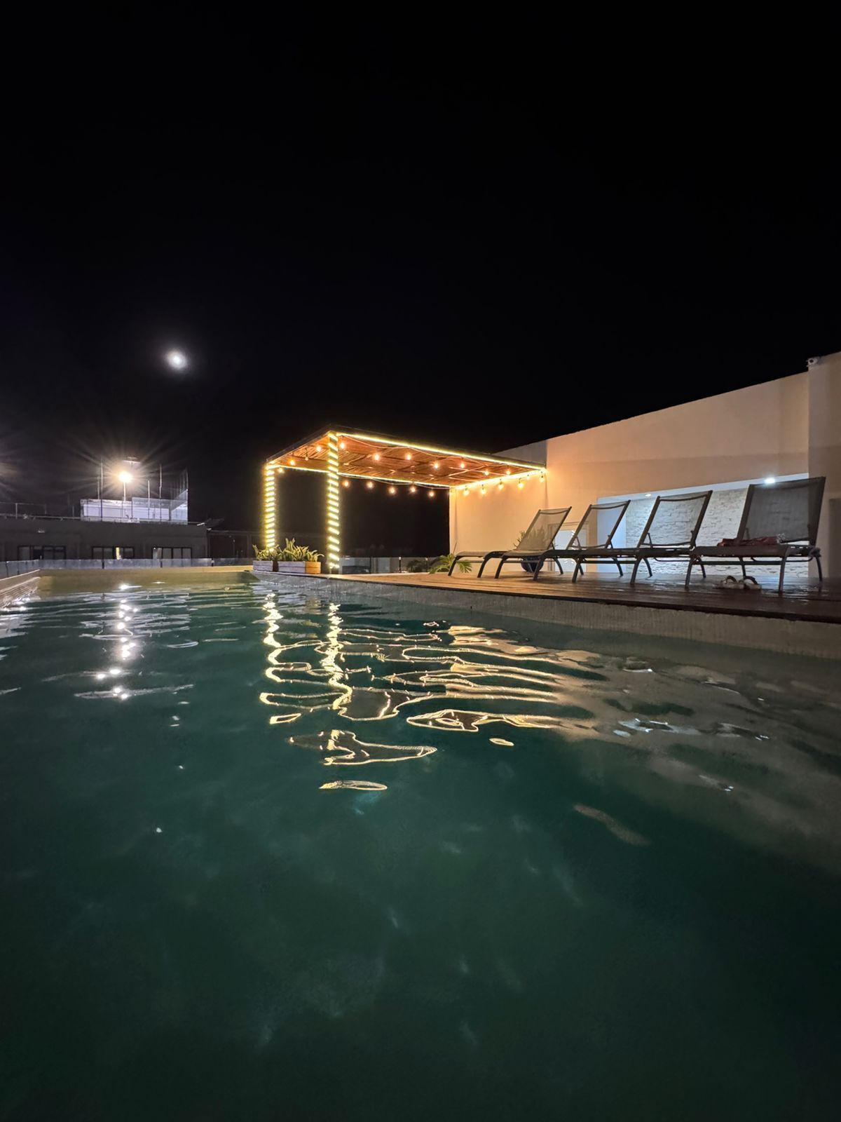 Ein Schwimmbecken bei Nacht mit überdachter Sitzgelegenheit und Lichterketten.