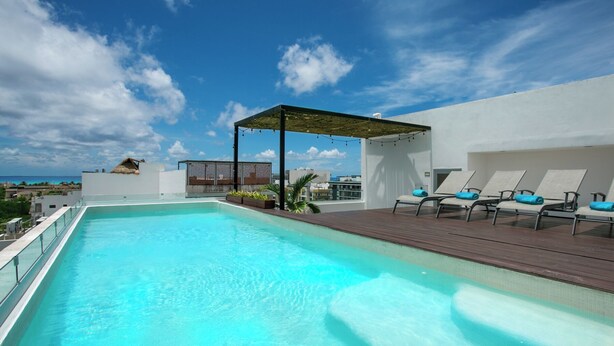 A rooftop pool with clear blue water, surrounded by lounge chairs and a pergola. - Your Home Away: Rooftop Pool Close to Beach & Fun (Playa del Carmen)
